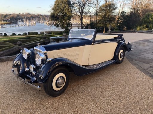 Classic convertible car in navy blue and cream parked by a scenic waterfront.