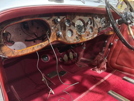 Classic car interior featuring wooden dashboard, vintage gauges, and red upholstery.